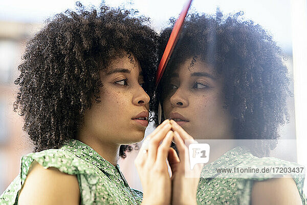 Young afro woman looking at reflection in glass wall