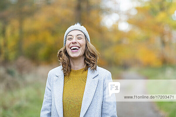 Happy woman with eyes closed laughing while standing in forest
