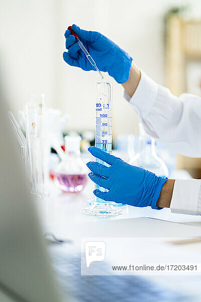 Die Hand einer Ärztin  die eine Lösung in einem Reagenzglas mit einer Pipette im Labor mischt