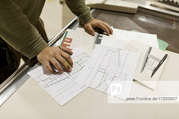 Männlicher Designer bei der Arbeit an einem handwerklichen Entwurf auf Papier  stehend an einer Werkbank in der Industrie