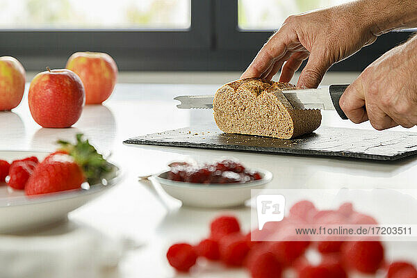 Hands of man cutting bread with kitchen knife