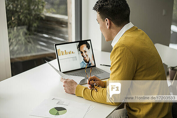 Geschäftsmann  der an einer Videokonferenz über einen Laptop teilnimmt  während er an seinem Schreibtisch im Heimbüro sitzt