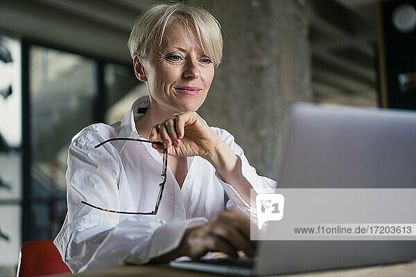 Lächelnde Geschäftsfrau mit Brille bei der Arbeit am Laptop im Büro zu Hause