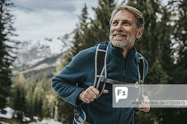 Lächelnder reifer Mann  der beim Wandern im Wald im Salzburger Land  Österreich  wegschaut