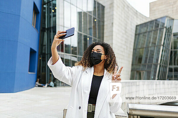 Frau  die während der COVID-19 ein Selfie mit ihrem Smartphone vor einem Gebäude macht