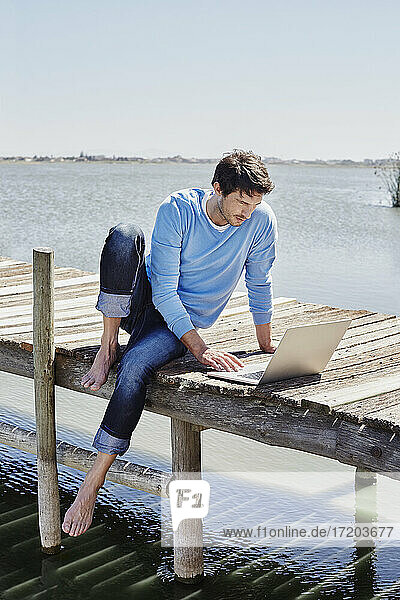 Mature man using laptop while sitting on pier