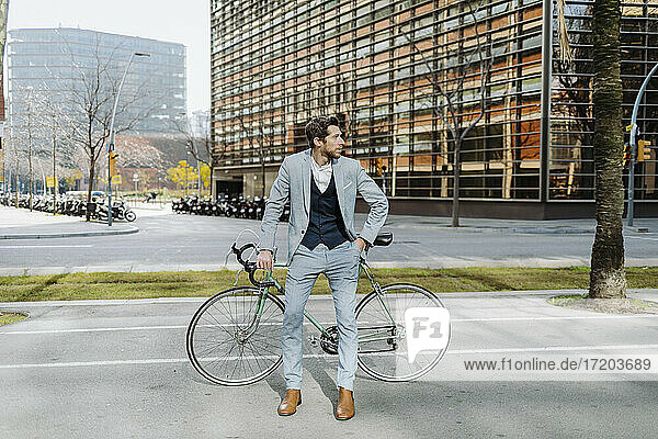 Männlicher Unternehmer mit Fahrrad steht in der Stadt und schaut weg