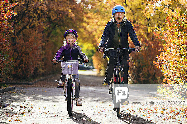 Glückliche Mutter und Tochter Radfahren auf der Straße im Park im Herbst