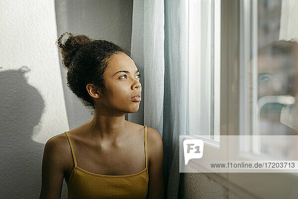 Nachdenkliche junge Frau  die durch das Fenster ihres Hauses schaut