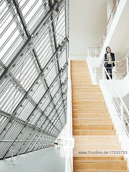 Weibliche Fachkraft steht an einem Geländer über einer Treppe im Büro