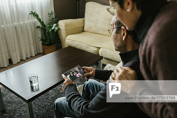 Ein älterer Mann und eine ältere Frau führen während der COVID-19 einen Videogespräch mit ihrer Familie über ihr Smartphone zu Hause