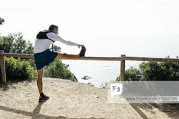 Man stretching on wooden railing during sunny day