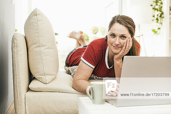 Mittlere erwachsene Frau mit Laptop auf dem Sofa im Wohnzimmer liegend