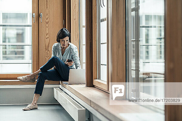 Geschäftsfrau arbeitet am Laptop  während sie im Büro am Fenster sitzt