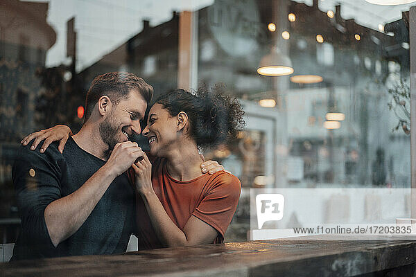 Couple smiling while sitting with arm around each other at cafe