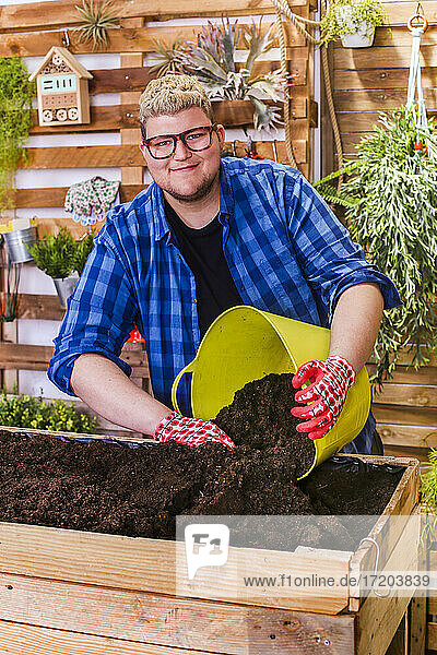 Junger Mann bereitet das Substrat für einen städtischen Garten aus Paletten auf seiner Terrasse vor