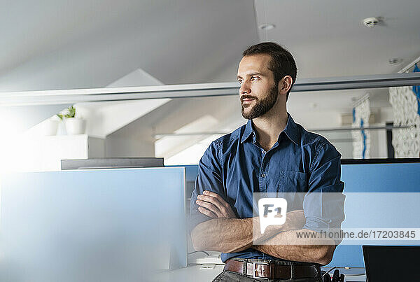 Businessman looking away while standing with arms crossed at office