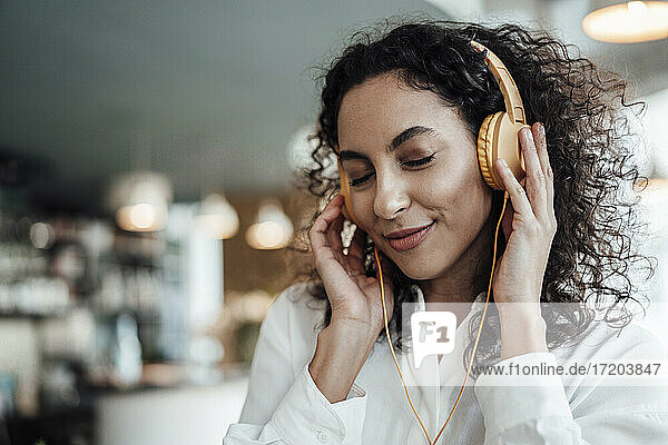 Smiling businesswoman listening music through headphones while standing at cafe
