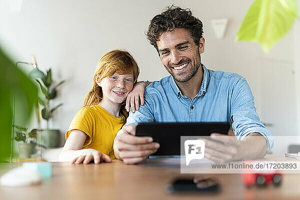 Vater mit rothaariger Tochter lächelnd und Blick auf digitale Tablette zusammen im Wohnzimmer