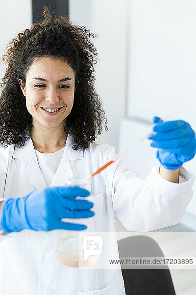 Lächelnde Ärztin  die im Chemielabor mit einer Pipette eine Lösung in einem Becherglas mischt