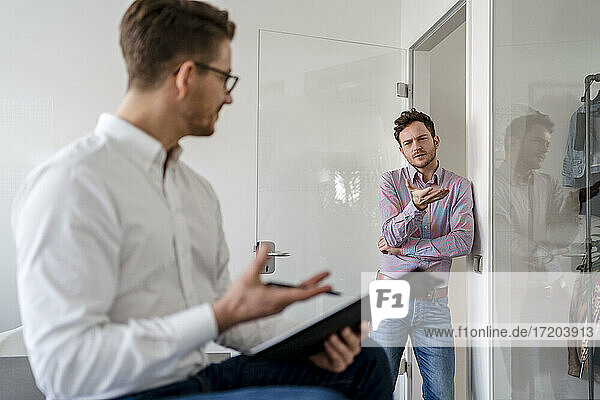 Businessman discussing with male colleague while leaning on door at office
