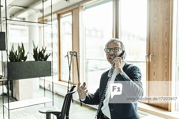 Businessman gesturing while talking on telephone in office corridor