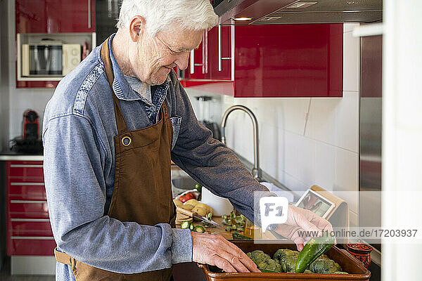 Älterer Mann beim Anrichten von Gemüse in der Küche zu Hause