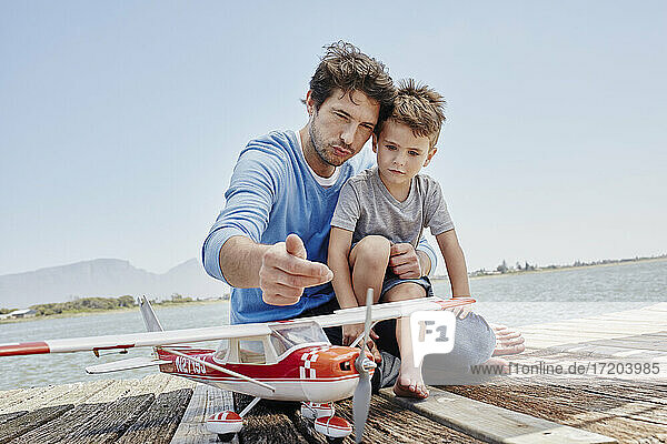 Vater spricht mit seinem Sohn über Flugzeugspielzeug  während er auf dem Pier sitzt