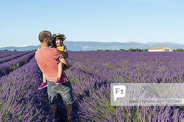 Father carrying baby daughter in vast lavender field during summer