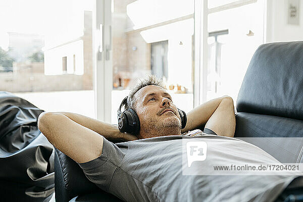 Mature man listening music through headphones while lying on sofa in living room