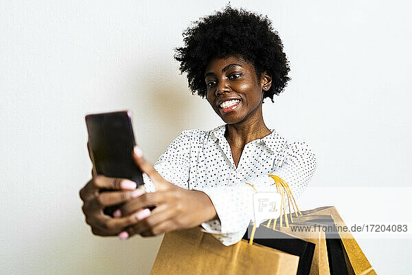 Lächelnde Frau  die ein Selfie mit ihrem Mobiltelefon macht  während sie vor einem weißen Hintergrund steht