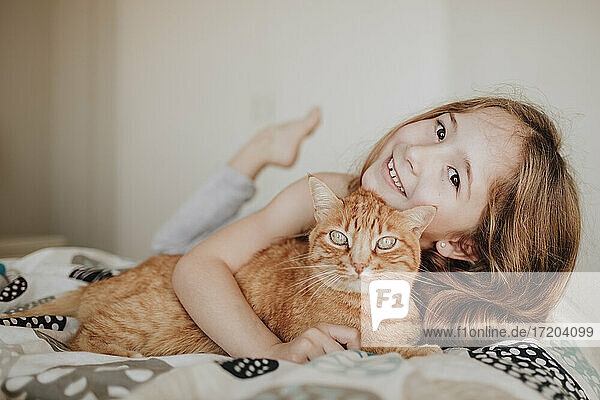 Nettes lächelndes Mädchen mit Ingwer Katze auf Bett zu Hause