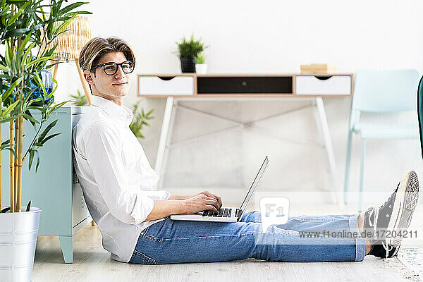 Entspannter Mann  der einen Laptop benutzt  während er zu Hause im Wohnzimmer sitzt