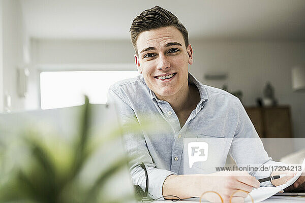 Smiling young businessman with document sitting at table in home office