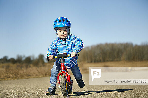 Junge schiebt beim Spielen mit dem Balance-Bike auf der Straße