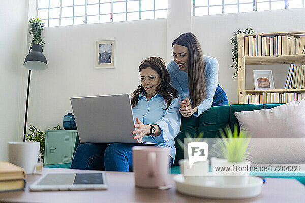 Reife Geschäftsfrau  die einen Laptop benutzt  während ihre Tochter auf dem Sofa im Heimbüro assistiert