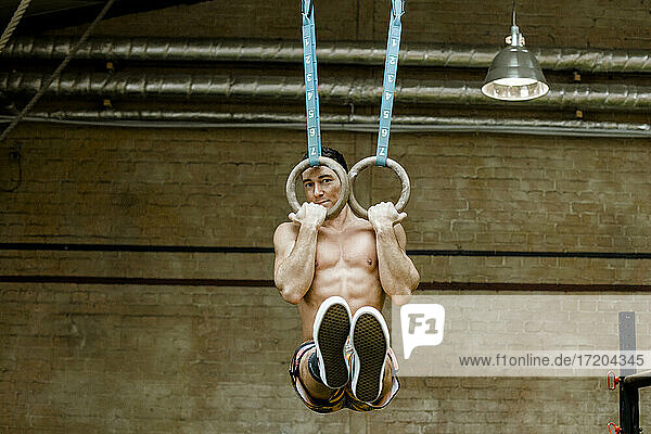 Hemdloser Mann hängt mit Gymnastikringen an der Wand im Fitnessstudio