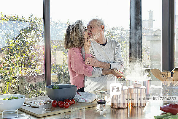 Älteres Paar  das sich küsst  während es an der Kücheninsel zu Hause steht