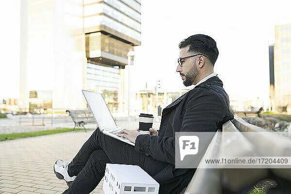 Male architect using laptop while sitting on bench in city