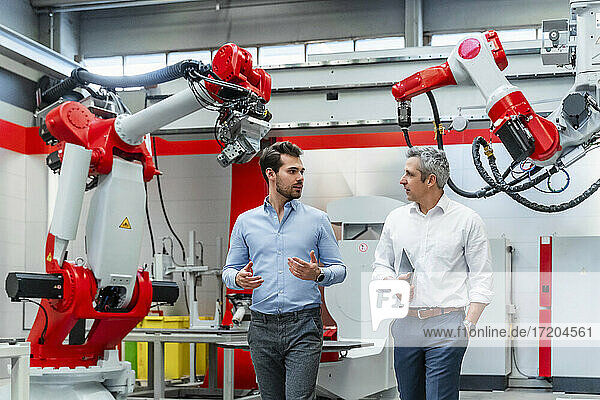 Young male automation engineer discussing with colleague against machinery in factory