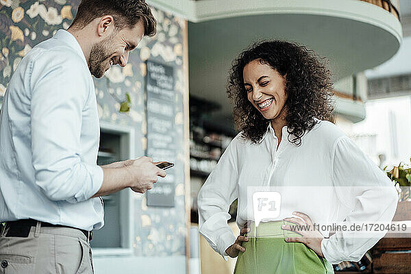Geschäftsmann  der ein Mobiltelefon benutzt  während er neben einem Kollegen im Café steht