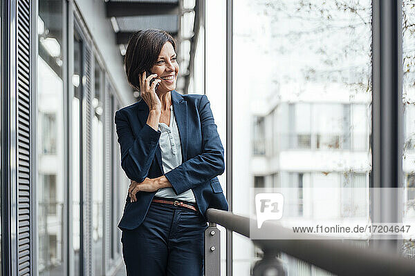 Glückliche Geschäftsfrau  die auf dem Bürobalkon mit einem Mobiltelefon spricht