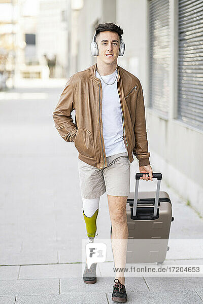 Hübscher junger Mann mit Behinderung zieht Gepäck auf dem Fußweg