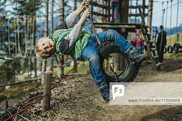 Verspielter Junge schwingt auf einer Reifenschaukel im Hochseilgarten im Wald