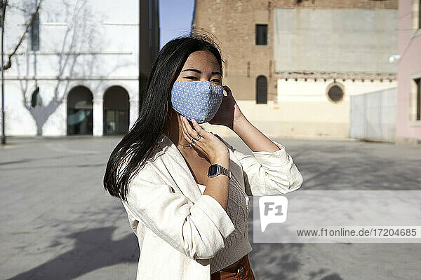 Junge Frau mit Gesichtsschutzmaske auf einem Fußweg an einem sonnigen Tag