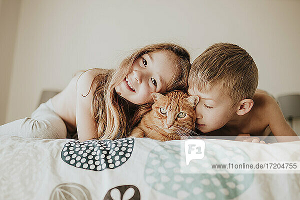 Lächelndes Mädchen mit Bruder  der sich auf eine Katze im Schlafzimmer stützt  zu Hause