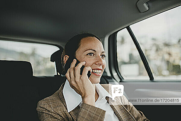 Lächelnde Unternehmerin  die während der Fahrt im Taxi telefoniert