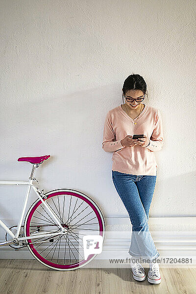 Lächelnde Frau  die ein Mobiltelefon benutzt  während sie zu Hause am Fahrrad steht