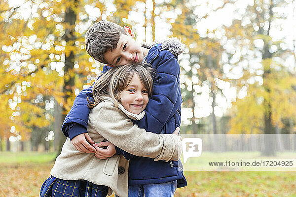 Lächelnder Bruder und lächelnde Schwester umarmen sich  während sie im Wald stehen