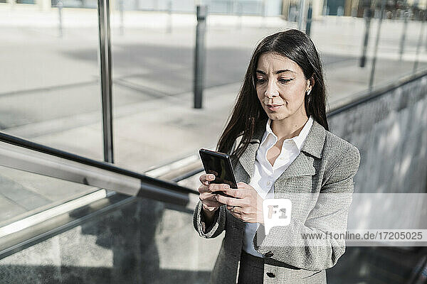 Geschäftsfrau  die ein Smartphone benutzt  während sie auf einer Rolltreppe in der Stadt steht